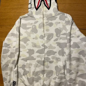 Vit camo hoodie med hajmotiv - Säljer min vita bape camo hoodie. Fick den i julklapp men den är lite för liten för mig. Använd bara 2 gånger.