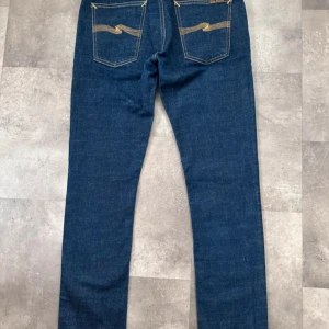 Blå jeans från Nudie Jeans - Snygga blå jeans från Nudie Jeans med klassisk femficksdesign och kontrastsömmar. De har en slim passform och är tillverkade i bomull med en liten del elastan för extra komfort. I nyskick och säljer för att dom inte passar mig. Hör gärna av er om frågor eller prisförslag!