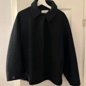 Kort kappa - Säljer denna korta kappa från COS. Medföljer även luva som man kan knäppa på om man vill!😇 Nypris ca 1700kr