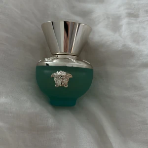 Turkos parfymflaska från Versace - Elegant parfymflaska i frostat turkost glas med silverdetaljer från Versace. Flaskan har en lyxig design med ett silverlock och den ikoniska Medusa-loggan i silver på framsidan. Perfekt för den som älskar exklusiva dofter och stilfull design. En fräsch och blommig doft. 30ml knappt använd 