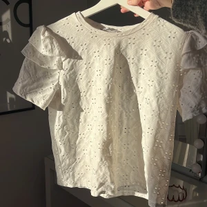 Vit blus från Zara - Säljer en söt vit blus från Zara med korta ärmar och volangdetaljer. Blusen har ett broderat mönster💓 kommer inte till användning längre, väldigt bra skick utöver att nån tråd sticker ut vid ett av broderierna, men det går att klippa bort om man vill men det syns inte så mycket och har aldrig tänkt på det förens nu när jag fel sökte plagget noga  