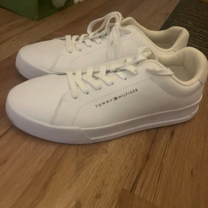 Vita skor från Tommy Hilfiger - Snygga vita sneakers från Tommy Hilfiger med klassisk design och snörning. Perfekta för en stilren look. Tillverkade i syntetmaterial med märkets logga på sidan. Har knappt används