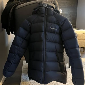 Peak Performance Frost Down - Säljer en marinblå dunjacka från Peak Performance. Jackan har en dragkedja framtill och en justerbar huva. Den är långärmad med elastiska muddar för extra värme. Inköpt i november men säljer den nu då jag letar efter något annat😊Väldigt sparsamt använd och har inga tecken på slitage (ex revor, hål eller fläckar). Inköp för 4200