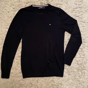 Merinoull tröja J Lindeberg  - Köp via PostNord! Storlek S. Tröjan är ny skick. Material :100% Merinoull. Marinblå  tröja från J.Lindeberg med rund hals och ett diskret vitt logotypbroderi på bröstet. Perfekt för en stilren look. Hör av er vid fler funderingar !