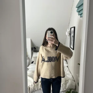 Beige tröja med text - Säljer en beige tröja med texten 'voila’ mörkblått på framsidan. Tröjan har en avslappnad passform och långa armar. Super känt material!