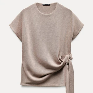 Beige topp med knyt från Zara - Snygg beige topp från Zara med korta ärmar och en stilren knytning i sidan. Perfekt för en chic och avslappnad look.