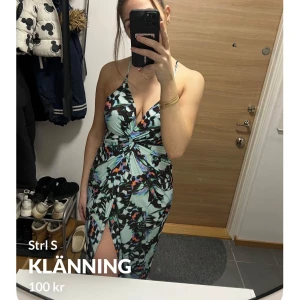 Blommig klänning med slits - Snygg blommig klänning med v-ringad design och smala axelband. Klänningen har en slits framtill och ett knyt i midjan som ger en fin passform. Perfekt för sommarens alla tillfällen!