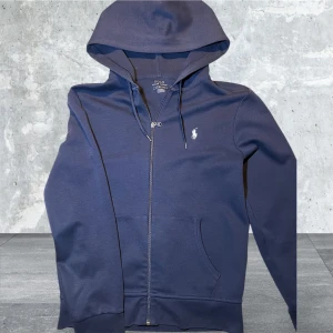 Kofta  från Polo Ralph Lauren |herr - Säljer en stilren mörkblå hoodie från Polo Ralph Lauren med dragkedja och huva. Den har en liten broderad logotyp på bröstet och praktiska fickor framtill. Perfekt för en fett outfit!