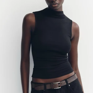 Svart ärmlös polotopp från Zara - Snygg svart ärmlös polotopp från Zara. Perfekt för en stilren look, med en tight passform som framhäver figuren. Tillverkad i mjukt material för extra komfort. Storlek M, använd enstaka gång. 
