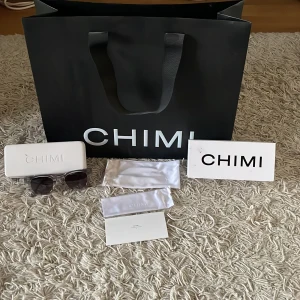 Grå solglasögon från Chimi 02 - Snygga grå solglasögon från Chimi med transparent båge och mörka linser. Perfekta för en stilren look. Kommer med originalförpackning och fodral.