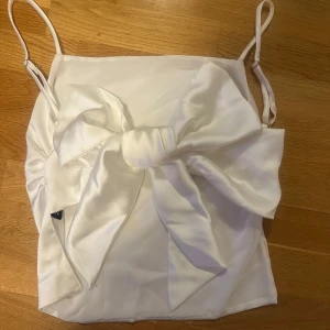 Vit topp med rosett - Säljer jättefin, slutsåld satintopp från Zara. Knappt använd och har knytning i ryggen. 