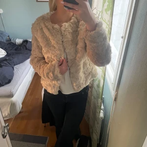 Beige pälsjacka - Säljer en supermjuk och fluffig beige pälsjacka. Jackan har en normal passform och långa ärmar, perfekt för att hålla sig varm och stilren. Den är enkel att matcha med olika outfits och ger en lyxig känsla.