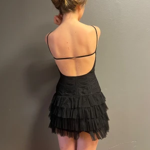 Svart klänning med volanger - Snygg svart klänning med smala axelband och volanger i flera lager. Den har en v-ringad design och en öppen rygg som ger en elegant look. Perfekt för en kväll ute eller en speciell tillställning. 🖤