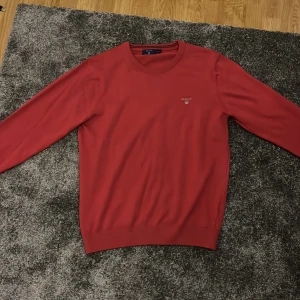 Röd tröja från GANT - Säljer en stilren röd tröja från GANT med rund halsringning och diskret logotyp på bröstet. Storlek M. Oanvänd. Röd/Rosa.