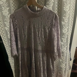 Ljuslila spetsklänning - Elegant ljuslila klänning i spets med trekvartsärm och hög hals. Perfekt för speciella tillfällen med sin romantiska design och fina detaljer. Klänningen har en vacker struktur och faller fint.