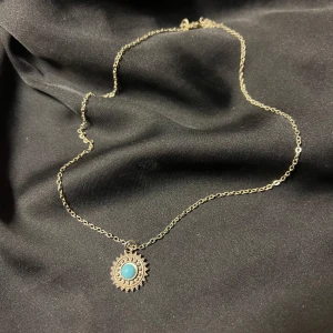 Halsband med turkos hängsmycke - Silverhalsband med ett runt turkost hängsmycke. Hängsmycket har en dekorativ kant som ger en bohemisk känsla. Ej äkta silver