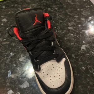 Nike Air Jordans i svart och rött - Snygga Nike Air Jordans i svart och rött med klassisk design. Skorna har en svart bas med röda detaljer och vit sula. Perfekta för en sportig look med ikonisk stil. PRIS KAN DISKUTERAS 
