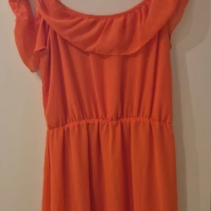 Orange klänning från BikBok - Säljer en härlig orange klänning från BikBok. Klänningen har en lös passform med volangdetaljer vid halsen och korta ärmar. Perfekt för sommarens varma dagar. 🌞