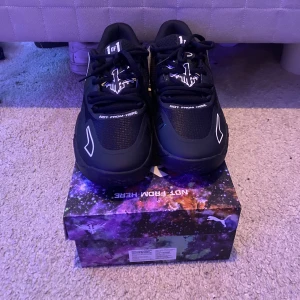 MB 1 Lo  - Snygga svarta basketskor från Puma med unikt vitt mönster på hälen och textdetaljer. Skorna har snörning och en futuristisk design med en färgglad låda. Perfekta för en modern och sportig look. Pris kan diskuteras vid snabb affär