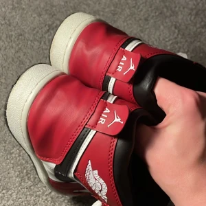 Nike Air Jordans i rött och vitt - Snygga Nike Air Jordans i rött och vitt med svart swoosh. Skorna har klassisk snörning och är perfekta för sneakerheads. De har en ikonisk design med Air Jordan-logga på sidan.