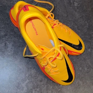 Gula fotbollsskor från Nike - Snygga gula fotbollsskor från Nike med svarta detaljer och snörning. Perfekta för fotbollsplanen med en iögonfallande design.