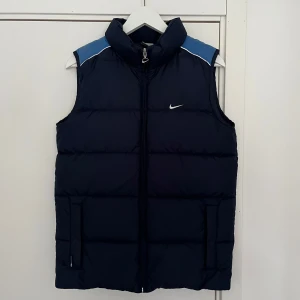 Mörkblå Nike dunväst - Varsamt använd, i mycket gott skick. Normal i storleken, ungefär som en XS i herr storlek.  Färgen är något ljusare i verkligheten. Den stämmer bäst överens med den tredje bilden. Meddela mig för fler bilder!