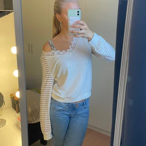 Vit och randig tröja med spetsdetaljer - Säljer en vit tröja med randiga ärmar och spetsdetalj vid halsringningen. Tröjan har en avslappnad passform och långa ärmar. Passar mig som vanligtvis bär storlek S.
