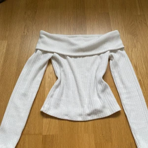 Vit offshoulder topp från Stradivarius - Säljer en stilren vit offshoulder topp från Stradivarius. Toppen är ribbad och har långa ärmar, vilket ger en elegant look. Perfekt för att klä upp eller ner beroende på tillfälle. Passar bra till både jeans och kjol💕