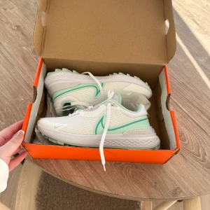 Vita och mintgröna Nike golfskor  - Snygga Nike golfskor i vitt med mintgröna detaljer. Skorna har en modern design med snörning och en bekväm sula. Perfekta för både träning och vardag.