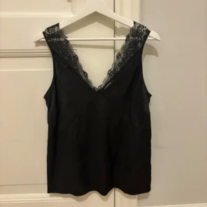 Svart topp från & Other Stories - Snygg svart topp från & Other Stories med spetsdetaljer vid axlarna. Aldrig använd och i perfekt skick! Storlek 34/XS.