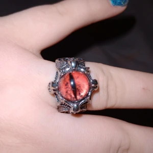 Ring med draköga - Unik ring med ett iögonfallande draköga i röd färg. Ringen har en detaljerad design med ett silverfärgat band som ger en mystisk och fantasy-inspirerad känsla. Perfekt för dig som vill ha ett smycke som sticker ut.