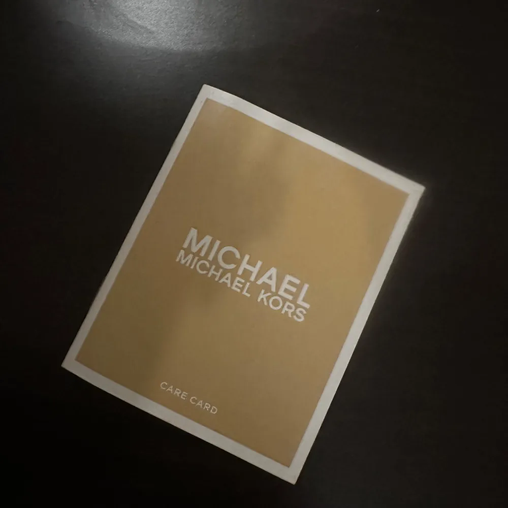 Snygg kuvertväska från Michael Kors i en stilren kombination av vitt och beige. Väskan har ett diskret mönster och en elegant logotyp i guld på framsidan. Perfekt för att bära det viktigaste med stil. Aldrig använd. . Laukut & Käsilaukut.