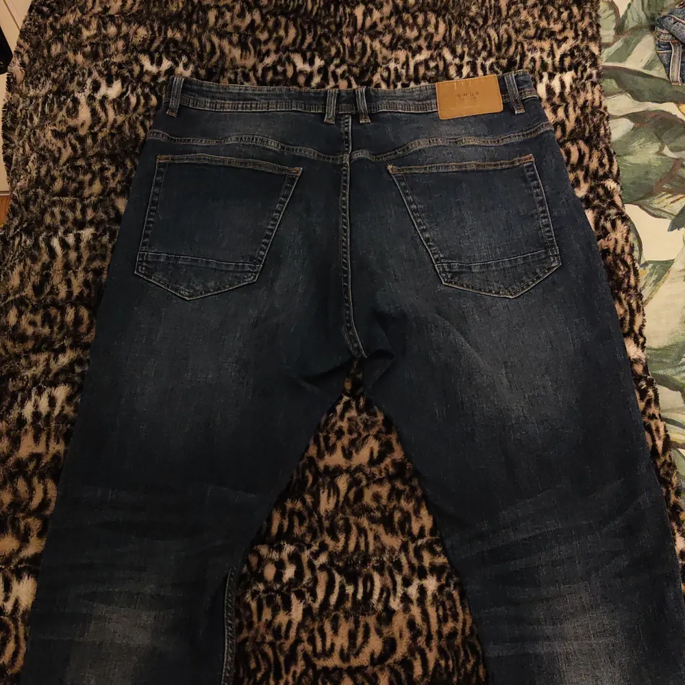 Snygga mörkblå jeans från Smog med klassisk femficksdesign och knappgylf. Jeansen har en lätt tvättad look och är perfekta för en avslappnad stil. Tillverkade i Bangladesh.. Farkut & Housut.