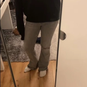Grå jeans med slitningar - Säljer ett par grå jeans med slitningar på knäna. De har en straight passform och är perfekta för en avslappnad stil. Jeansen har en klassisk design med fem fickor och knappgylf. Jeansen är bootcut och är ifrån Gina tricot. Modellen är low waist. 🫶