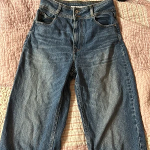 Blå jeans från Zara - Säljer ett par sköna blå jeans från Zara med hög midja och raka ben. De har en knappgylf och femficksdesign. Supersköna att ha på sig! Midjemåttet tvärs över är 36 cm och innerbenet är ca 65 cm