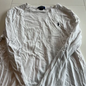 Vit långärmad tröja från Polo Ralph Lauren - Säljer en klassisk vit långärmad tröja från Polo Ralph Lauren med det ikoniska broderade logotypen på bröstet. Perfekt för en stilren och avslappnad look. Tröjan är i mjukt bomullsmaterial och har en rund halsringning.