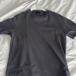 Grå t-shirt från Prada - Snygg grå t-shirt från Prada med en diskret logga på bröstet. Perfekt för en stilren look. T-shirten har korta ärmar och en klassisk passform.