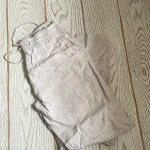 Beige linnebyxor med snörning - Snygga beige linnebyxor med elastisk midja och snörning för extra komfort. Perfekta för en avslappnad stil med en lätt och luftig känsla. Byxorna har en rak passform och är idealiska för varmare väder. Använda 2 gånger 