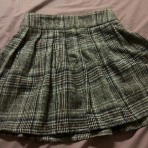 Rutig kjol från NLY Trend - Snygg rutig kjol från NLY Trend i grå toner. Kjolen har en klassisk design med veckad stil och är perfekt för en stilren look. Den är kort och passar bra till olika tillfällen. Ett måste i garderoben för den som gillar tidlös stil.