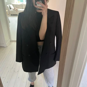 Svart kavaj från Hugo Boss - Snygg svart kavaj från Boss med klassisk design och dubbelknäppning. Perfekt för en stilren look. Kavajen har en elegant passform och är tillverkad i ett material som ger en lyxig känsla.