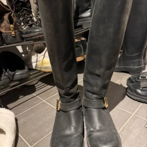 Johnny bulls  - Snygga svarta stövlar i skinn med dekorativa spännen och dragkedja baktill. 