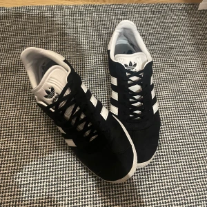Adidas Gazelle sneakers - Snygga Adidas Gazelle sneakers,  Skorna har den klassiska tre-randiga designen i vitt på sidan och Adidas-loggan på hälen. De är tillverkade i mocka med snörning framtill och en vit sula. Riktigt bra skick 9/10 storlek 42
