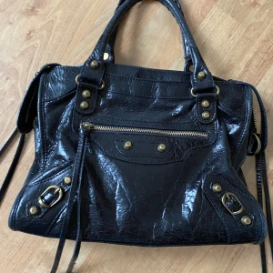 Klassisk svart city bag i äkta läder - Såå fin klassisk city bag i äkta genuine leather, lite glansigt patent distressed leather look!! Med fransar, spegel och axelrem!! Perfekt som skolväska! Är lite mindre än den klassiska storleken, denna e 30cm bred! Studs och metalldetaljer i brass-aktig nyans!!