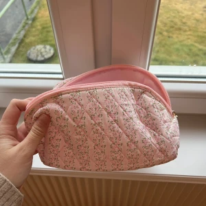 Rosa quiltad necessär med blommönster - Söt rosa necessär med quiltat mönster och små blommor. Den har en dragkedja i guld och är perfekt för att förvara smink eller andra småsaker. Den är kompakt och lätt att ta med sig.