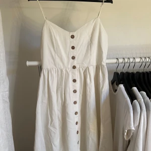 Vit sommarklänning - Vit lång sommarklänning med knappar framtill och band som man kan ställa in själv. Använd en gång och säljer pågrund av att den inte är min stil längre. Kommer från Zaful.