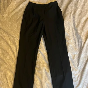 Svarta kostymbyxor från H&M - Snygga svarta kostymbyxor från H&M med hög midja och rak passform i benen. Använda en gång, mycket bra skick. Säljes pågrund av att dom inte kommer till användning. 