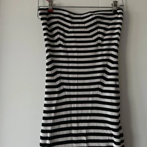 Randig tubklänning från Gina Tricot - Snygg randig midi- tubklänning från Gina Tricot i svart och vitt. Klänningen är axelbandslös och har en ribbad struktur som ger en cool look. 🤍🖤🤍