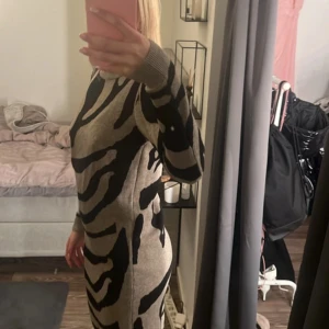 Zebramönstrad klänning - Snygg zebramönstrad klänning i beige och svart med långärmad design. Perfekt för en trendig look. Klänningen har en tight passform som framhäver figuren.
