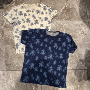 Två palm-mönstrade t-shirts från Kappahl - Säljer två snygga t-shirts från Kappahl med palm-mönster. En i marinblått och en i beige/vit, båda med korta ärmar. Perfekta för en avslappnad stil. Nyskick, endast använts två gånger. 
