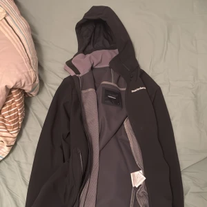 Svart jacka från Peak Performance - Snygg svart jacka från Peak Performance med huva och dragkedja. Perfekt för kyligare dagar med sin stilrena design och praktiska fickor. Jackan har en sportig look och är idealisk för både vardag och utomhusaktiviteter.